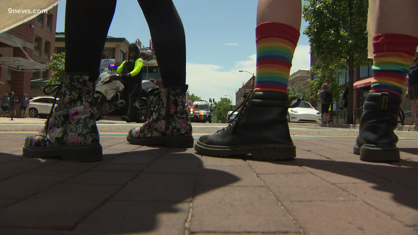 A photo of boots standing on the Pearl Street mall in Boulder. One of the pairs of boots has a flower print and the other has rainbow socks.